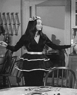 a woman in a black dress is standing in front of a table with plates and chairs .