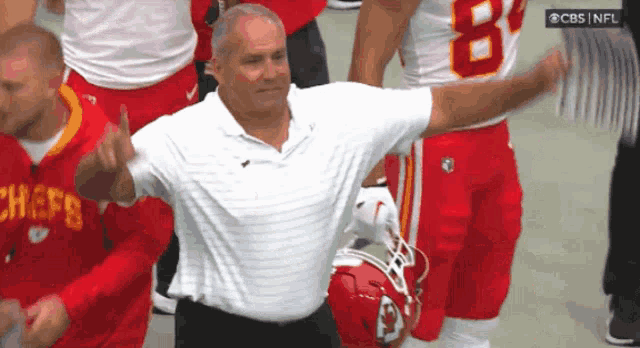 a man wearing a chiefs shirt stands in front of a group of players