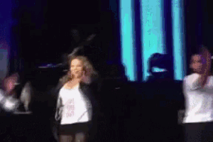 a group of people are dancing on a stage with a blue light behind them .
