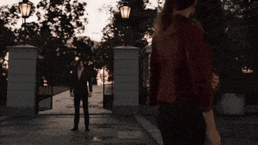 a man in a suit and a woman in a red jacket are standing in front of a gate that says 19803leon on it