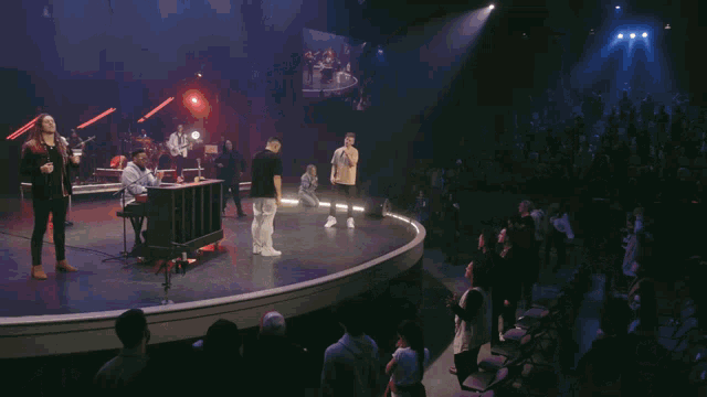 a group of people singing on a stage in front of a large screen