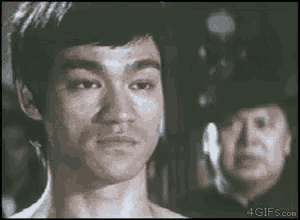 bruce lee is looking at the camera while a man in a police hat looks on .