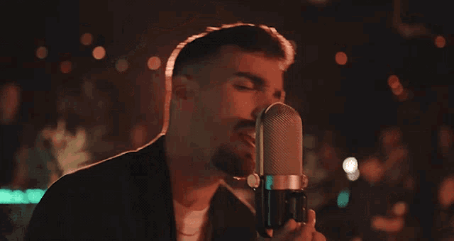 a man singing into a microphone with ay written on the bottom right