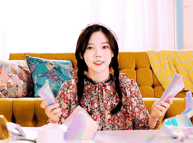 a girl is sitting on a yellow couch holding a book