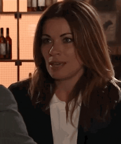 a woman in a black jacket and white shirt is talking to a man in a bar