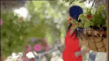 a woman in a red dress is standing in front of a planter with flowers .