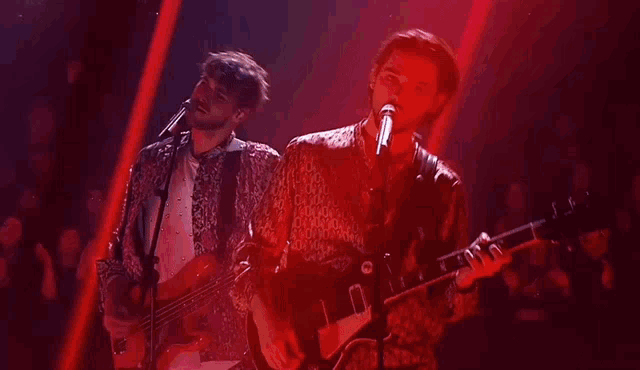 a man singing into a microphone while another man plays a guitar in front of a crowd