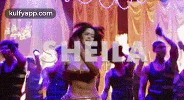 a woman is singing into a microphone while a group of people are dancing in front of her .
