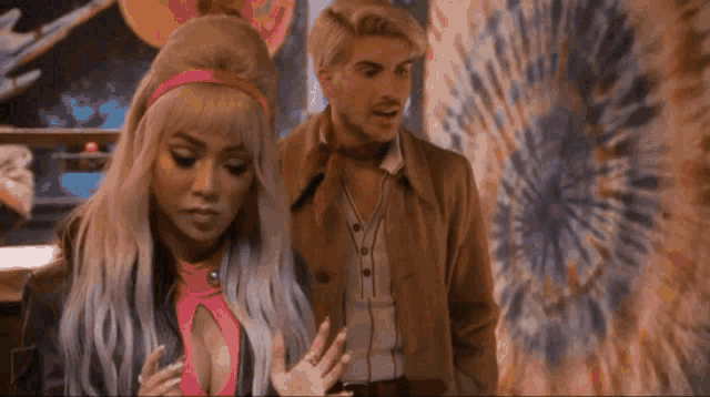 a man and a woman are standing next to each other in front of a tie dye painting .