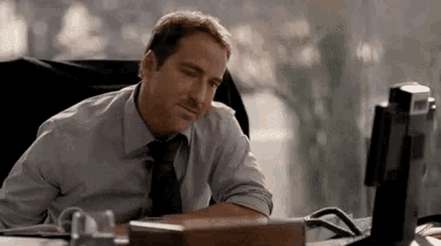 a man in a shirt and tie is sitting at a desk in front of a computer .