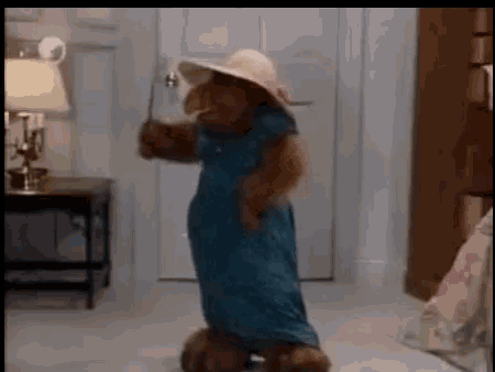 a teddy bear wearing a blue dress and hat is dancing in a bedroom