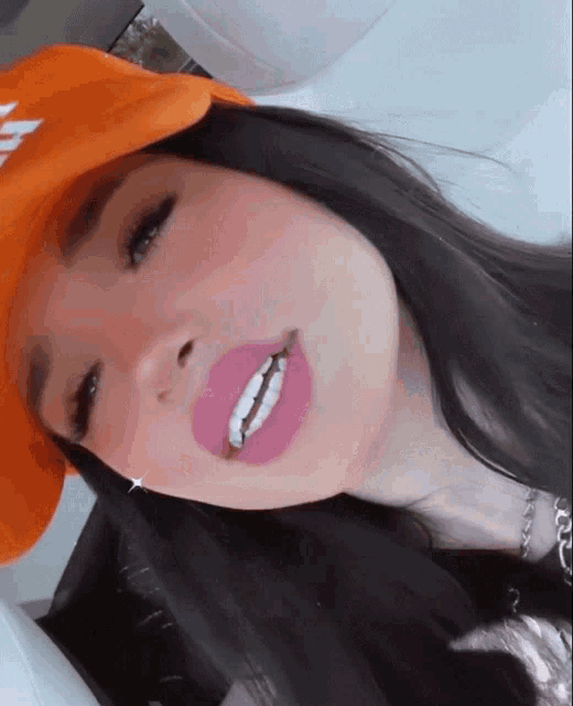 a woman wearing an orange hat and pink lipstick smiles