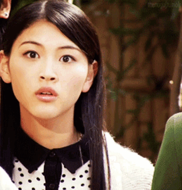 a woman wearing a polka dot shirt and a white sweater is looking at the camera