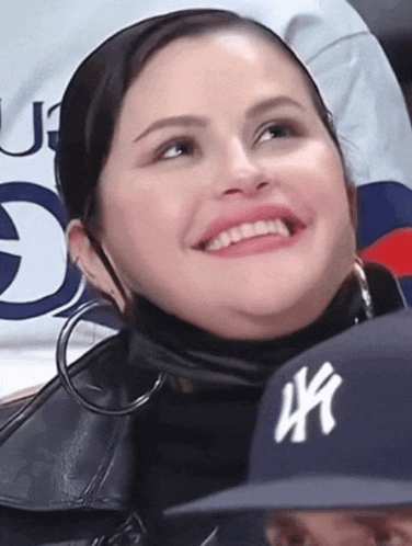 a woman wearing a new york yankees hat smiles in the stands