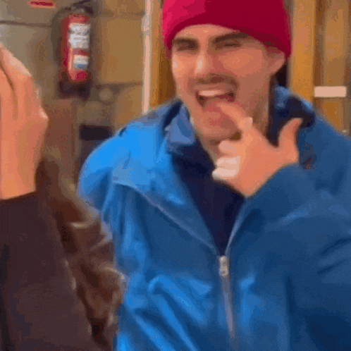 a man in a blue jacket and red hat is making a funny face .