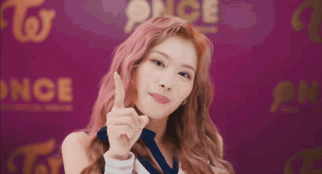 a close up of a woman with pink hair giving a thumbs up sign .