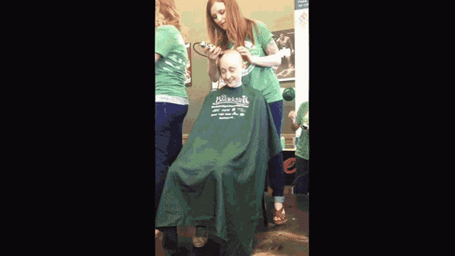 a woman is cutting a man 's hair and he is wearing a shirt that says masters