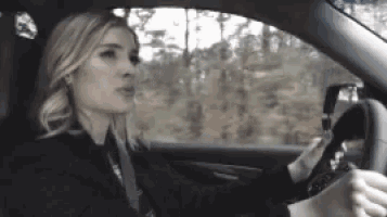a woman is driving a car and looking at the rear view mirror .
