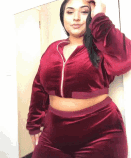 a woman is standing in front of a mirror wearing a burgundy velvet tracksuit .