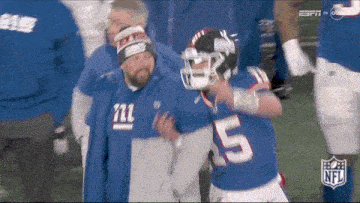 a new york giants football player is being helped off the field by a man wearing a giants hat .