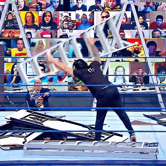 a man in a wrestling ring is holding a ladder in front of a crowd that is watching a wrestling match
