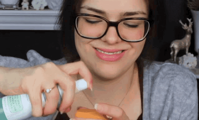 a woman wearing glasses and a ring is spraying something on her neck