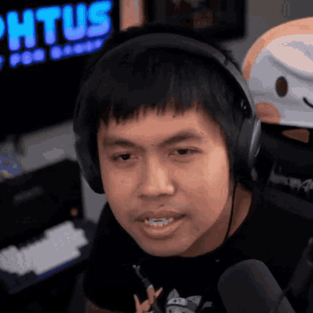 a man wearing headphones looks at the camera in front of a sign that says phtus