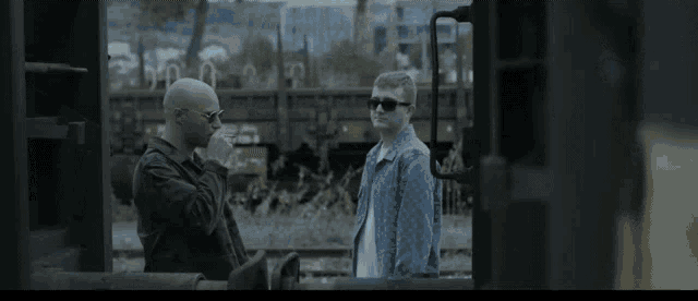 two men are standing next to each other on a train track
