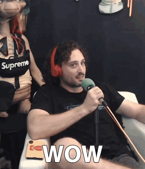 a man wearing headphones and a supreme shirt is holding a microphone and says wow