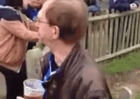 a man is drinking from a plastic cup while another man holds a bottle .