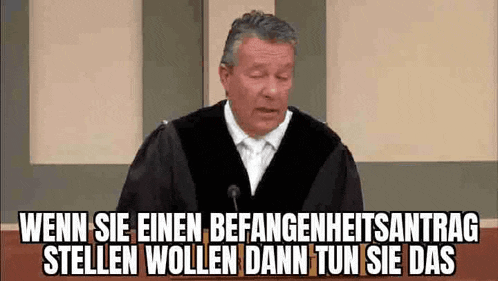 a man in a judge 's robe stands in front of a microphone and says wenn sie einen befangenheitsantrag