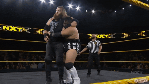 a wrestler is hugging another wrestler in a ring with the word nxt on the bottom