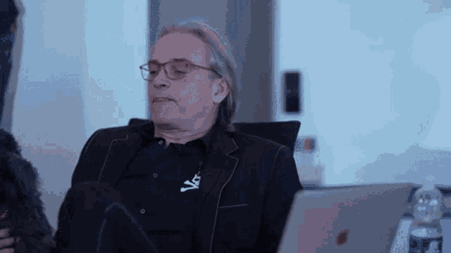 a man wearing glasses is sitting in front of a laptop and a bottle of water