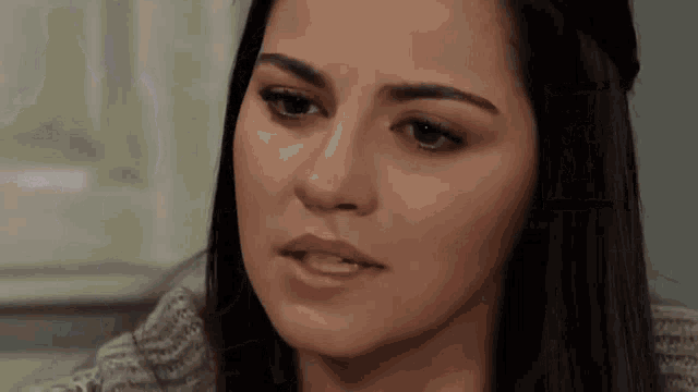 a woman with long dark hair is wearing a grey sweater
