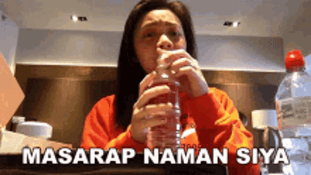 a woman in a red sweatshirt is drinking water from a bottle with the words masarap naman siya written below her