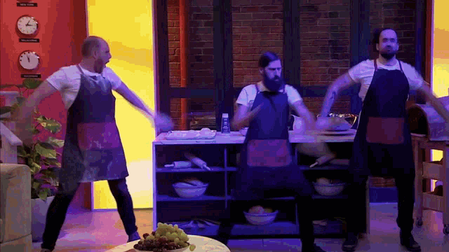 a group of men in aprons are dancing in a kitchen with clocks on the wall behind them