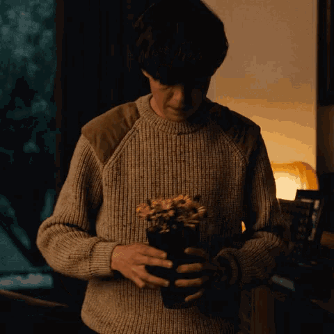 a man in a sweater is holding a potted plant of flowers