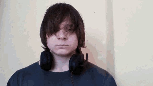 a young man wearing headphones around his neck looks at the camera