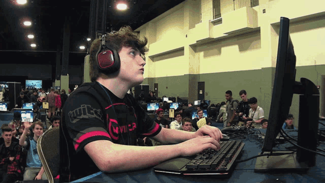 a man wearing headphones and a shirt that says twitch is typing on a computer