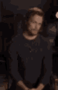 a man in a black shirt is standing in a dark room with his fist in the air .