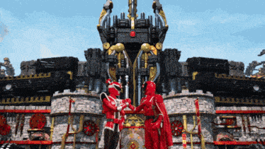 a couple of red robots shaking hands in front of a large building