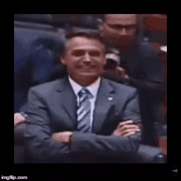 a man in a suit and tie is smiling while sitting in a chair with his arms crossed .