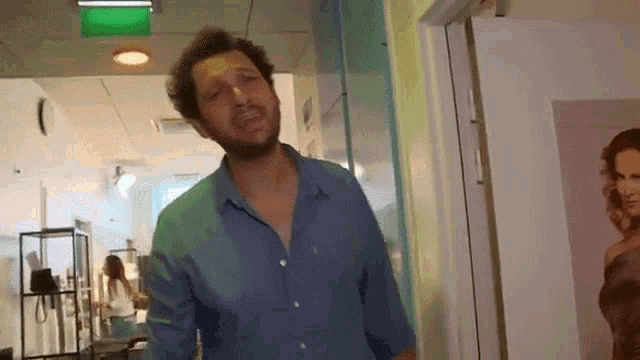 a man in a blue shirt is standing in a room with a picture of a woman on the wall
