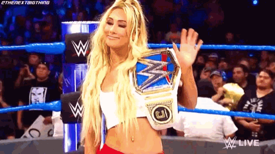 a woman in a wrestling ring is holding a championship belt and waving at the crowd .
