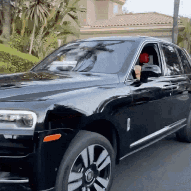 a black rolls royce is parked on the street in front of a house
