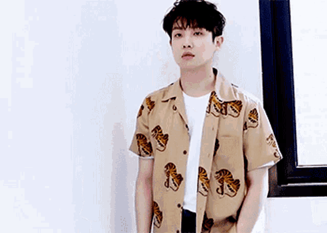 a young man is standing in front of a window wearing a tiger print shirt .