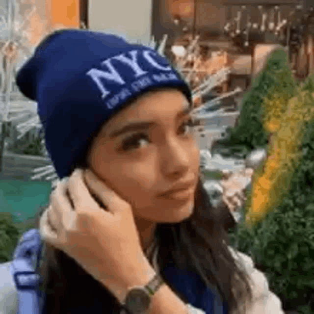 a woman wearing a blue beanie with nyc written on it is talking on a cell phone .