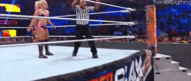 a referee is standing in the middle of a wrestling ring while two women wrestle .
