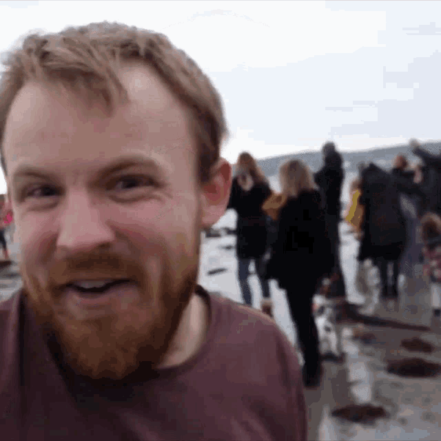 a man with a beard is smiling in front of a crowd on a beach
