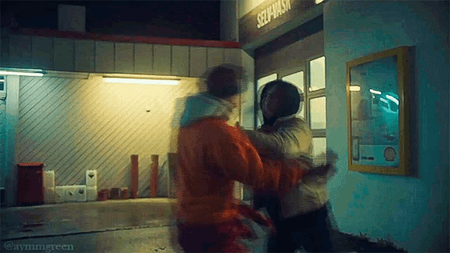 two people are fighting in front of a building that has the word self wash on it